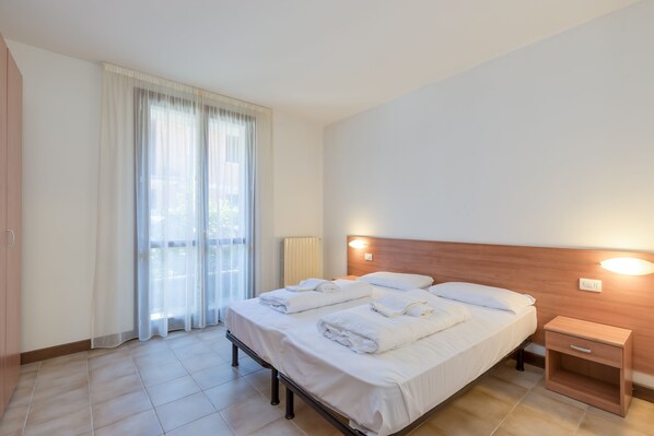Une chambre d’hôtel avec un lit double, deux tables de chevet, une commode et une grande fenêtre avec des rideaux.