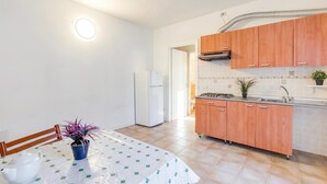 Een keuken met houten kastjes, een witte koelkast, een fornuis en een eettafel met tafelkleed.