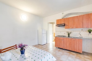 A kitchen with wooden cabinets, a white refrigerator, a stove, and a dining table with a tablecloth.