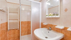 Een badkamer met een douchecabine van glas, een wit wastafeltje en een spiegel met verlichting.