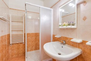 A bathroom with a glass shower enclosure, a white sink, and a mirror with lights.