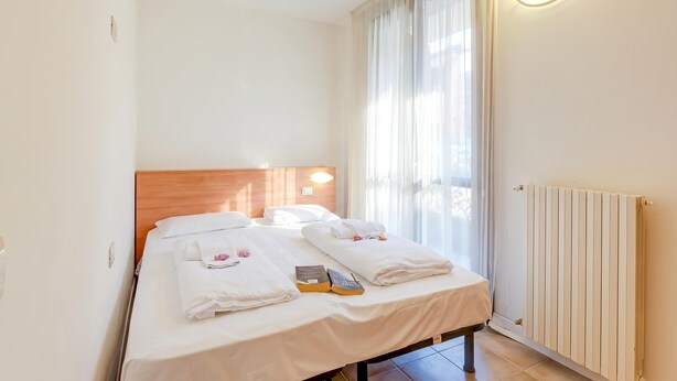 Een hotelkamer met twee bedden, een houten hoofdbord, een nachtkastje, een radiator en een raam met gordijnen.