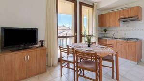 A compact kitchen with wooden cabinets, a dining table with chairs, a flat-screen TV, and a balcony with a view.