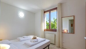 A hotel room with a bed, a bedside lamp, a window with curtains, a mirror, and a radiator.