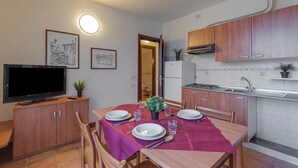 A dining area with a table set for four, a television on a cabinet, and kitchen cabinets. - Porto Letizia Chopin 9, Porlezza, Italy (Porlezza)