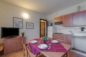 Un coin repas avec une table dressée pour quatre personnes, un téléviseur posé sur un meuble et des placards de cuisine.