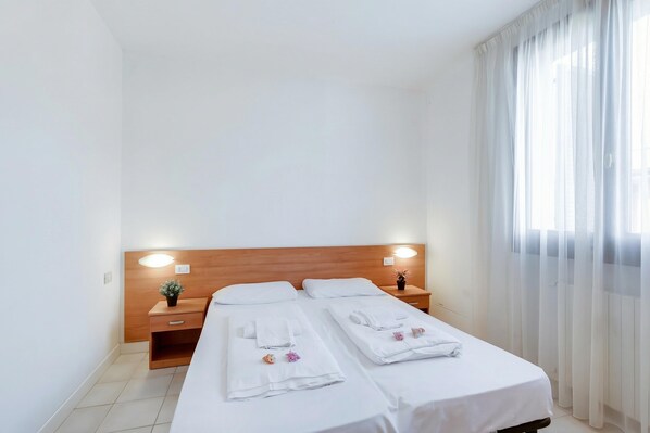 A hotel room with two beds, a wooden headboard, bedside lamps, a small plant, and a window with sheer curtains. - Porto Letizia Chopin 8, Porlezza, Italy (Porlezza)