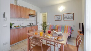 Uma cozinha compacta com armários de madeira, uma mesa de jantar com cadeiras, uma televisão e um sofá com manta listrada.