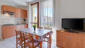 Cocina compacta con mesa, sillas, televisor y balcón con cortinas.