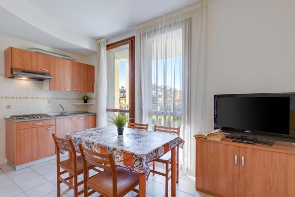 Une cuisine compacte comprenant une table à manger, des chaises, un téléviseur et un balcon avec des rideaux.