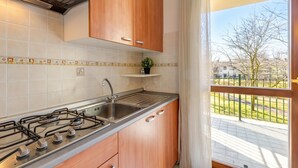 Una cocina con estufa a gas, pileta, alacenas de madera y vista a un balcón.