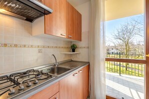 A kitchen with a gas stove, sink, wooden cabinets, and a view of a balcony.