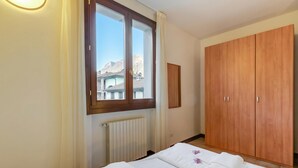 A bedroom with a large window, a wooden wardrobe, a radiator, and a neatly made bed. - Porto Letizia Chopin 6, Porlezza, Italy (Porlezza)