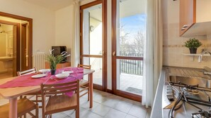 A dining area with a table set for two, a kitchen with a gas stove, and a sliding glass door leading to a balcony. - Porto Letizia Chopin 6, Porlezza, Italy (Porlezza)