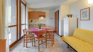 A compact living space with a dining area, kitchenette, and a yellow sofa. - Porto Letizia Chopin 6, Porlezza, Italy (Porlezza)