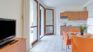Una cuina moderna amb armaris de fusta, una taula de dinar amb caires taronja i una televisió sobre un suport de fusta.