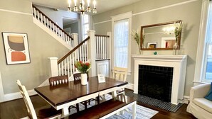 Une salle à manger avec une table et des chaises en bois, un escalier, une cheminée et un coin salon avec un canapé.