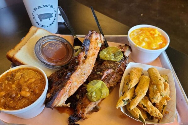 A tray with grilled fish, bread, a bowl of chili, a container of sauce, and a bowl of macaroni and cheese.