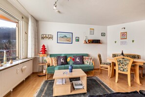 A living room with a green sofa, a wooden coffee table, a dining table with chairs, and a radiator.