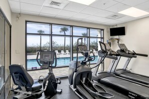 A gym with treadmills, elliptical machines, and a pool view.