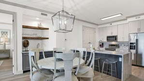 Een moderne keuken met witte kastjes, een centraal kookeiland met barstoelen, een magnetron en een roestvrijstalen koelkast.