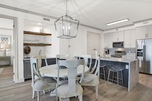 A modern kitchen with white cabinetry, a central island with bar stools, a microwave, and a stainless steel refrigerator.