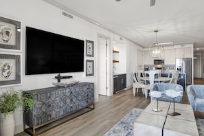 A modern living room with a large flat-screen TV, a geometric-patterned console table, and a dining area with a white table and chairs.