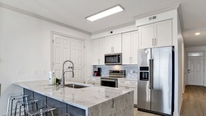 Een moderne keuken met witte kasten, roestvrijstalen apparatuur en een marmeren eiland met barstoelen.