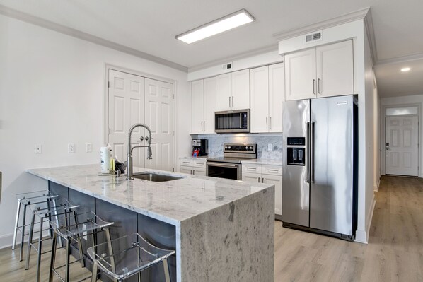 A modern kitchen with white cabinets, stainless steel appliances, and a marble island with bar stools.