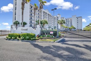 A hotel entrance with a sign reading "Grand Pointe," surrounded by palm trees and a well-maintained garden.
