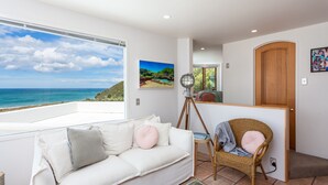 A room with a white sofa, a wicker chair, a wooden door, and a view of the ocean. - Santorini style, luxury apartment, stunning views! (Bowentown)