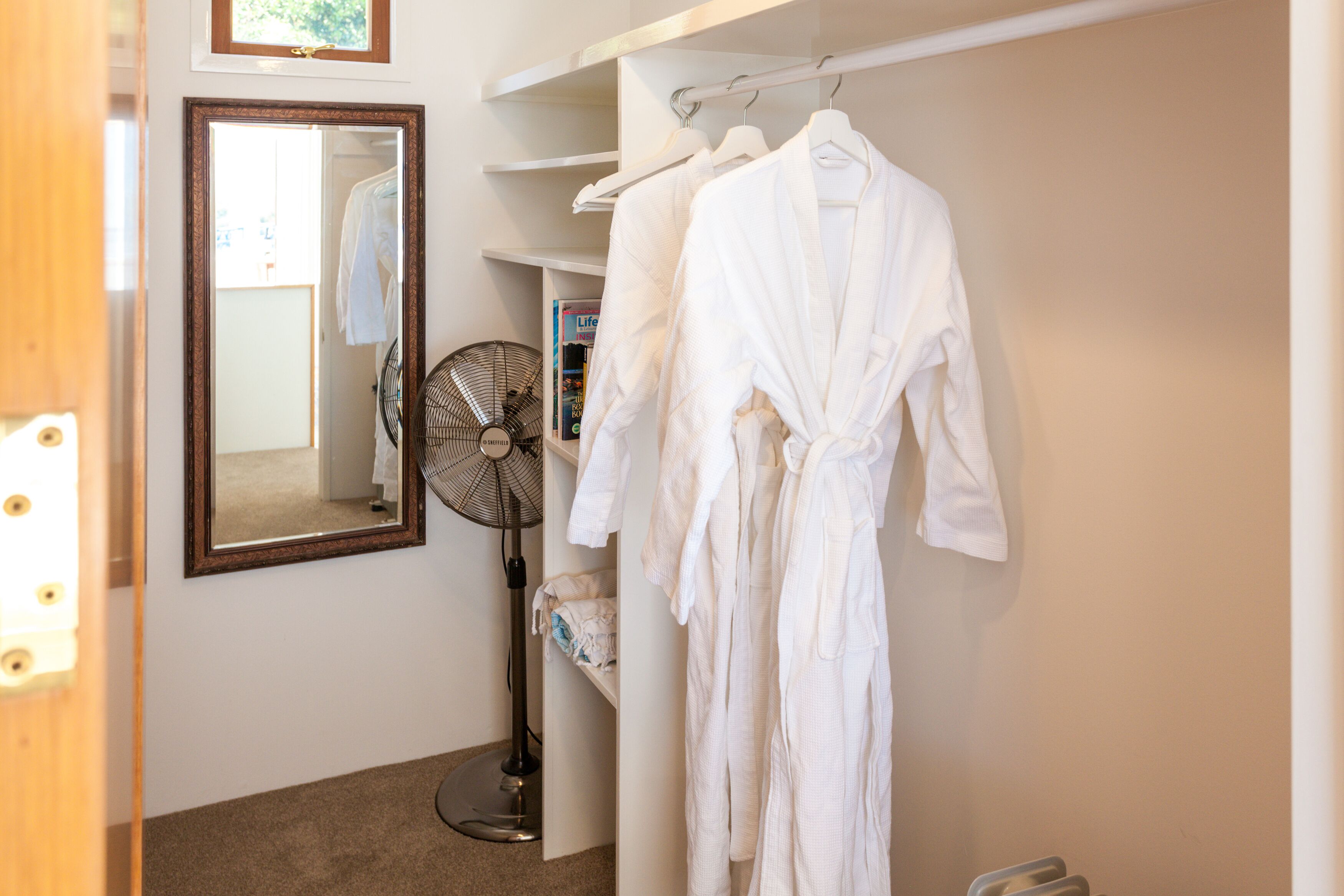 A bathroom with a mirror, a fan, and a rack with white robes.