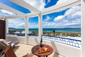 A balcony with a table set for two, a bottle of wine, and a cheese board.
