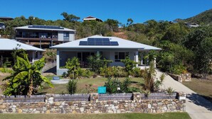 Een modern huis met zonnepanelen, omgeven door een stenen muur en weelderig groen.