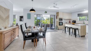 Une cuisine moderne avec un coin repas, comprenant un grand îlot central, des tabourets de bar et une vue dégagée grâce aux portes vitrées.