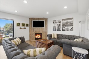 A modern living room with a fireplace, grey sofas, a TV, and cityscape wall art.
