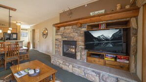 A living room with a stone fireplace, a flat-screen TV, wooden furniture, and a stone accent wall. - Walk to Ski, Large 2 Bed 2 Bath Near Lifts 459 (Mammoth Lakes)