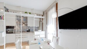 Une cuisine moderne avec des meubles blancs, une table à manger pour deux personnes et un téléviseur à écran plat fixé au mur.