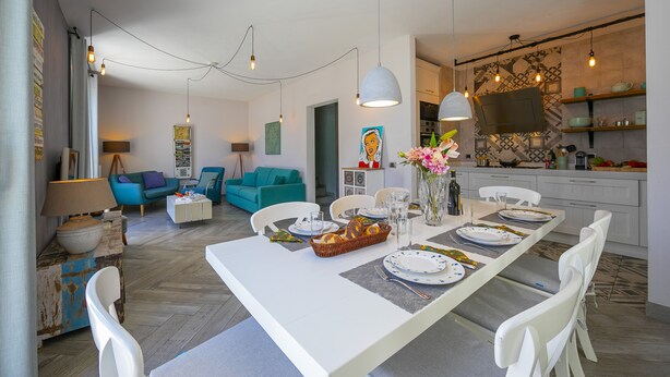 A modern living room with a dining area, featuring a long table set for a meal, a sofa, and a TV in the background. - Porto Letizia Primula 1, Porlezza, Italy (Porlezza)