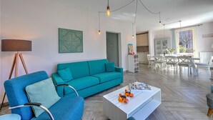 A modern living room with a teal sofa, a white coffee table, and a dining area in the background. - Porto Letizia Primula 1, Porlezza, Italy (Porlezza)