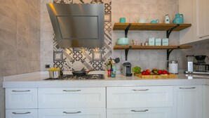 A modern kitchen with white cabinetry, a stainless steel range hood, and wooden shelves with kitchenware. - Porto Letizia Primula 1, Porlezza, Italy (Porlezza)