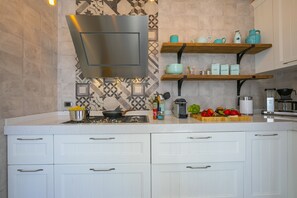 A modern kitchen with white cabinetry, a stainless steel range hood, and wooden shelves with kitchenware.