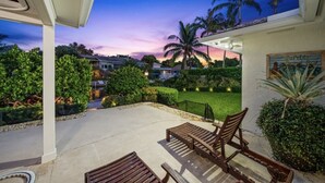 A patio area with wooden furniture, a well-maintained lawn, and a view of the sunset. - Jupiter waterfront - dock and new  jacuzzi spa , 3 b 2 b fits 30 “ boat   (Jupiter)