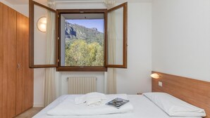 Une chambre à coucher avec un lit, une fenêtre avec des rideaux, une armoire en bois et un luminaire fixé au mur.