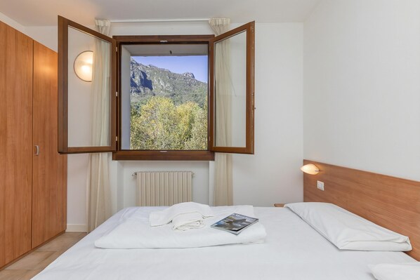 Une chambre à coucher avec un lit, une fenêtre avec des rideaux, une armoire en bois et un luminaire fixé au mur.