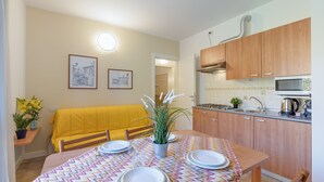 Une cuisine compacte avec des meubles en bois, une table à manger dressée avec des assiettes et des verres, et un canapé jaune en arrière-plan.