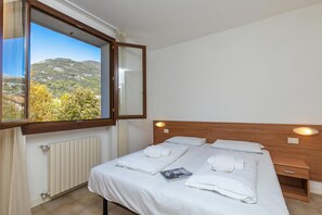 Une chambre avec une grande fenêtre, une tête de lit en bois, une table de chevet et un radiateur.