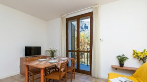 Une pièce comprenant une table à manger, des chaises, un téléviseur, un canapé et un balcon agrémenté de plantes.