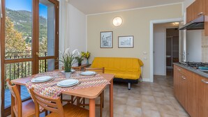 Un coin repas avec une table dressée pour quatre personnes, un canapé jaune et une cuisine dotée de meubles en bois et d’une cuisinière.