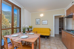 Un'area pranzo con un tavolo apparecchiato per quattro persone, un divano giallo e una cucina con un fornello.